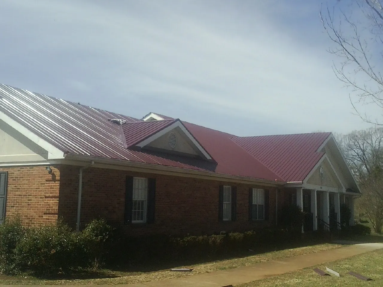 Red metal roof with gabled entries on a long brick building, from a Hail Damage Roof Repair job in Radnor