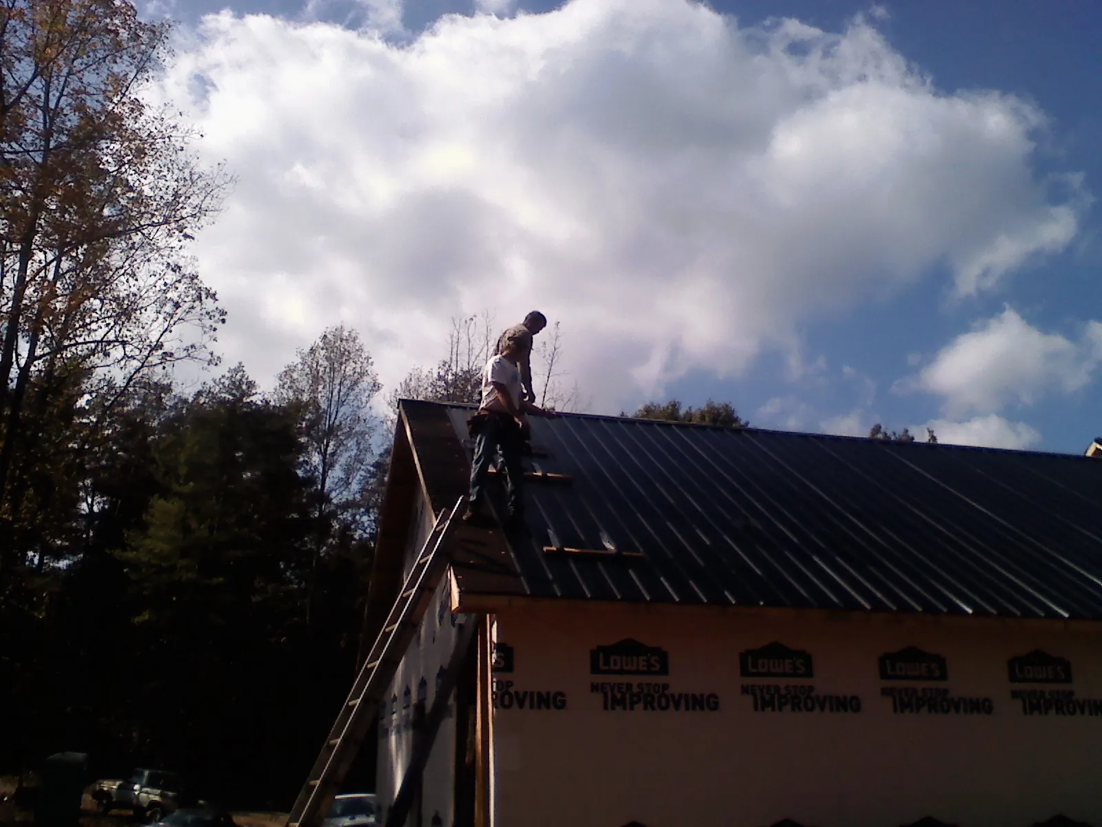 Roofer fastening dark metal panels high against a cloudy sky, from a Roof Inspection job in Radnor