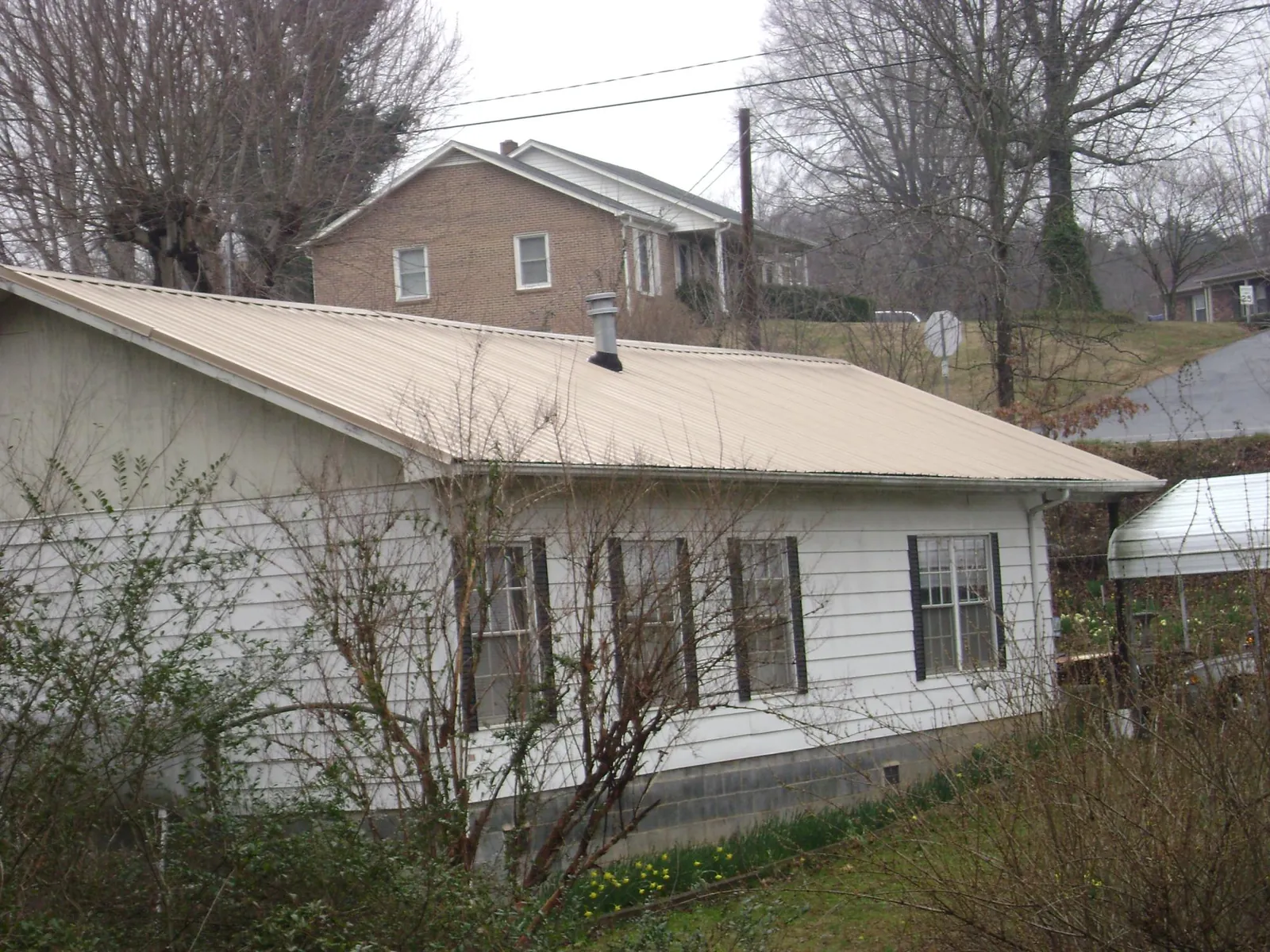 Tan metal roof on a white sided house set into a hillside — Commercial Roofing by Roofing Brothers in Radnor